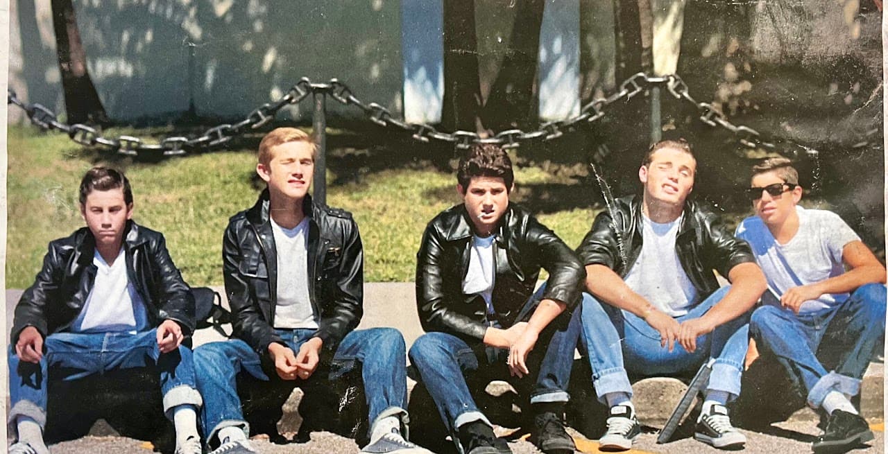 Ryan and his closest friends sitting on a low wall in matching jackets, looking like a James Dean photograph